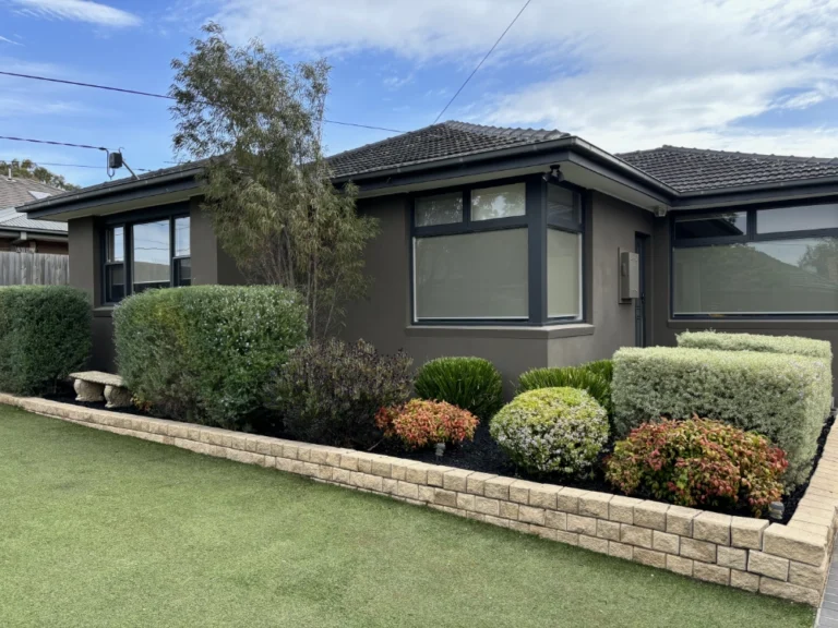 A front angle view of a house with a grass lawn, retainer wall and manicured lawns.